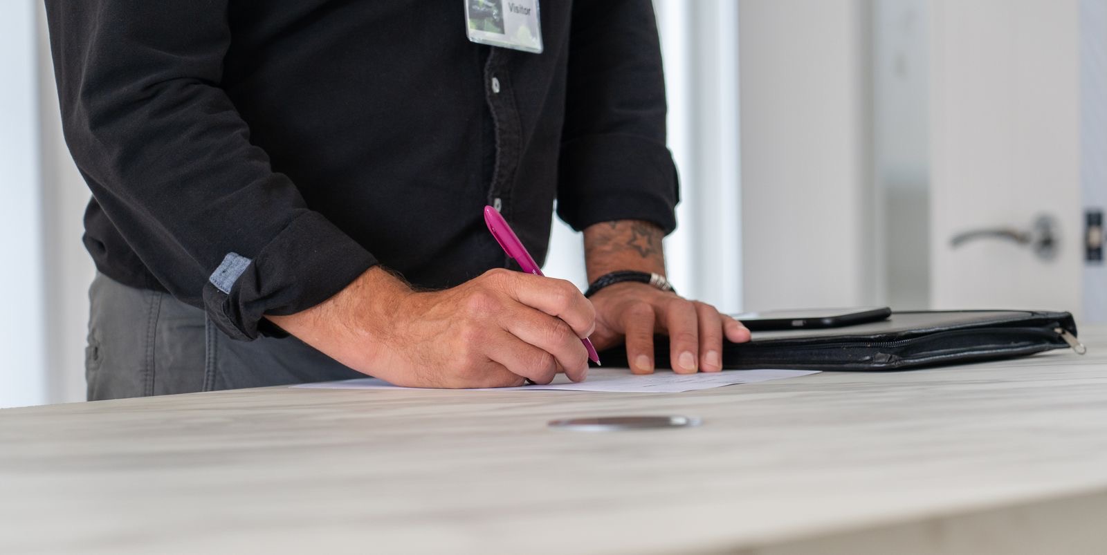 A new employee signing onboarding papers at a desk, an identity card face down beside the form.